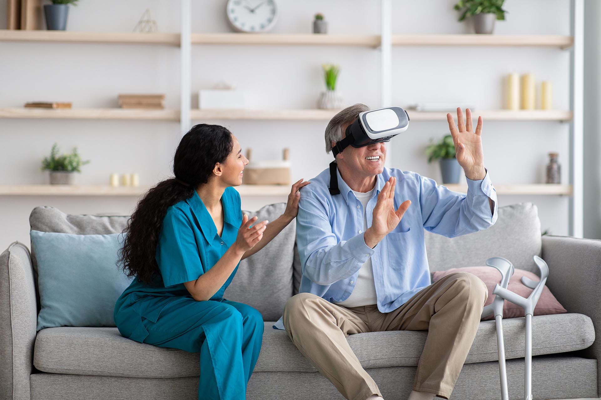 Disabled senior man using VR headset with young nurse, exploring augmented reality at home. Elderly male patient with doctor playing virtual game, having fun with futuristic technologies